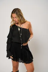 Blusa negra con un hombro descubierto y manga larga con volados.