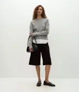 Suéter de punto jaspeado en color gris oscuro, con cuello redondo y mangas largas. Presenta un diseño integrado con una camisa blanca debajo, creando un efecto de capas superpuestas.