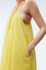 Vestido maxi solero amplio y largo de color amarillo, con escote redondo, frunces que otorgan vuelo, breteles finos ajustables con nudo en los hombros y bolsillos laterales.