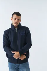 Campera de felpa azul marino con cuello alto, cierre frontal y bolsillos laterales. Tiene un logo estampado en el pecho.