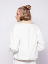 Campera de jean azul con interior forrado en corderito color crema. Presenta cuello camisero, cierre frontal con botones metálicos y dos bolsillos frontales con solapa.