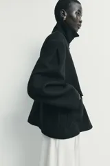 Abrigo corto de paño con mezcla de lana, color negro. Presenta cuello subido con cierre de botones, manga larga y dos bolsillos de plastrón con solapa en el frente. Cierre frontal con botones.