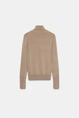 Jersey de punto liso en color beige, con cuello alto y manga larga con detalle de botones metálicos en los puños.