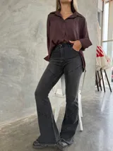 Pantalón de jean color gris oscuro con corte acampanado, tiro alto y costuras decorativas horizontales en las piernas. Presenta un ruedo deshilachado.