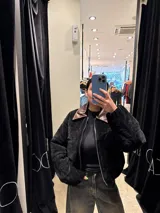 Chaqueta de pana negra con diseño acolchado, cierre frontal y cuello de solapa en cuero sintético marrón.