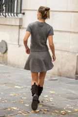 Botín de mujer de serraje color marrón oscuro, estilo motero, con caña media y tres tiras ajustables con hebillas metálicas plateadas. Posee tacón de bloque medio y tirador trasero para facilitar el calce.