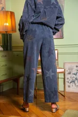 Pantalón azul con estampado de estrellas brillantes, de corte recto y fluido, cintura alta con trabillas para cinturón, cierre con botón y cremallera, bolsillos laterales.