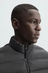 Chaleco acolchado verde oscuro, con cuello alto, cierre frontal con cremallera y bolsillos laterales. Confeccionado en tejido técnico repelente al agua.