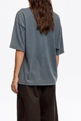 Remera de corte oversize color gris oscuro con efecto lavado, cuello redondo y manga corta amplia. Presenta un estampado pequeño de un perro salchicha con el logo de la marca en el pecho.
