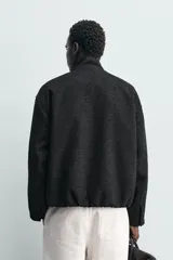 Cazadora de corte regular con cuello subido y cierre frontal de cremallera. Presenta un diseño de tejido jacquard con textura geométrica, manga larga, bolsillos de vivo en la cadera y bolsillo interior.