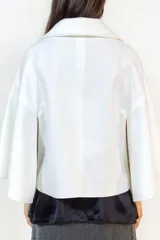 Capa corta de paño en color blanco, con diseño de doble botonadura frontal y cuello solapa. Presenta mangas amplias y corte holgado que aporta movimiento y sofisticación.