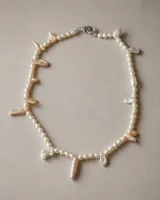 Collar de perlas de diversas formas, tamaños y matices, con diseño irregular y cierre metálico.