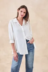 Camisa de corte holgado y fluido, color blanco, con cuello clásico, cierre frontal de botones y mangas tres cuartos con puños rectos.