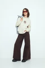 Canguro negro de calce relajado con capucha y cordones ajustables. Presenta un estampado gráfico frontal de un ojo con rayos de sol y la frase "STAY WEIRD".