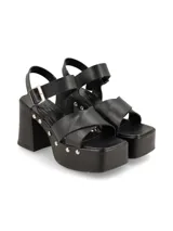Sandalia de plataforma color negro, con taco ancho, tiras cruzadas en el empeine y tira al tobillo con hebilla ajustable. Cuenta con detalles de tachas metálicas en los laterales de la plataforma y el talón.