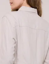 Sobrecamisa beige de lino liviano, con cuello camisero, cierre frontal de botones carey y bolsillos en el pecho. Cuenta con cordón ajustable en la cintura y mangas largas.