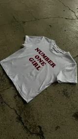 Remera crop top blanca de manga corta, con estampa frontal en color bordó con la frase "Number One Girl".