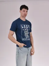 Remera azul petróleo de algodón con estampa rectangular en el frente con la palabra "LOST" en la parte superior, una serpiente enrollada en el centro y la frase "FEEL GOOD NEVER ENOUGH" en la parte inferior.