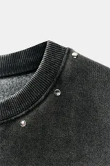 Sudadera de cuello redondo y manga larga, color gris oscuro con efecto lavado. Presenta aplicación de tachas metálicas alrededor del cuello y estampado frontal con el texto "CALIFORNIA USA" en blanco.