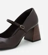 Zapato estilo Mary Jane de poliuretano color marrón oscuro, con punta redondeada, tira con hebilla ajustable sobre el empeine y taco bloque de altura media con acabado símil madera.