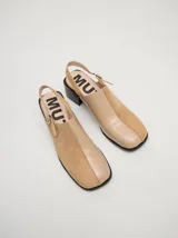 Zuecos de cuero vacuno con acabado en charol, color beige. Presentan un diseño clásico con taco cuadrado de madera de 5 cm y correa trasera ajustable con hebilla metálica.