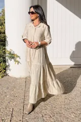 Vestido largo de estilo camisero en color azul, con cuello clásico, cierre frontal de botones y mangas tres cuartos con trabillas. Presenta un diseño de falda con cortes horizontales que le otorgan volumen y movimiento.