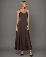 Vestido largo estilo lencero color chocolate, con breteles finos, escote en V y caída fluida. Presenta recortes geométricos en el frente y aberturas laterales con detalles de encaje. Confeccionado en tela satinada.