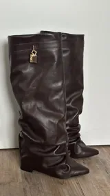 Botas de caña alta color marrón chocolate, de cuero vegano, con punta fina y detalle de candado dorado en la parte superior.