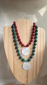 Collar doble de cuentas, uno con cuentas rojas estriadas y el otro con cuentas turquesas jaspeadas, ambos terminados con un dije colgante circular de nácar blanco.