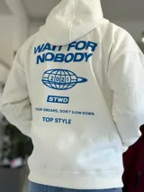 Canguro oversize blanco con capucha y bolsillo tipo canguro, confeccionado con tela de felpa suave. Presenta estampado azul en la espalda con la inscripción "WAIT FOR NOBODY", un diseño de planeta con el año 2021, el logo "STWD" y las frases "CHASE YOUR DREAMS, DON'T SLOW DOWN" y "TOP STYLE".