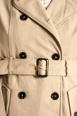Trench impermeable de corte oversize en color camel, con diseño de doble botonadura, solapas clásicas y cinturón ajustable en la cintura.