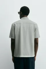 Camisa de manga corta color verde grisáceo, de corte regular fit, confeccionada en tejido suave y elástico con cierre de botonadura frontal.