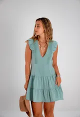 Vestido corto color verde agua, con escote en V profundo, volados en los hombros y detalle de encaje vertical en el frente. Presenta una falda con cortes horizontales que le otorgan movimiento.