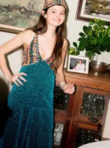 Vestido largo sin mangas con escote en V halter y aberturas laterales (cut-outs) en la cintura. El cuerpo superior presenta un llamativo diseño estampado multicolor, mientras que la falda larga es de tejido texturizado brillante en color verde esmeralda con inserciones godet en el ruedo.