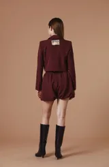 Saco tipo spencer negro de corte corto y estructurado, con solapas clásicas y detalles de pines decorativos distribuidos en la parte frontal.