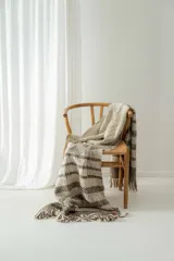 Manta tejida a crochet con diseño a rayas horizontales en tonos crudo y marrón, con flecos en los extremos.