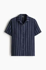Conjunto de pijama de dos piezas compuesto por una camisa de manga corta con cuello abierto y botones, y un short con cintura elástica y cordón de ajuste. Presenta un diseño a rayas verticales en tonos azul marino.