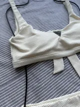Top de bikini entero color crudo, con textura y abertura triangular en el centro del busto. Se ata en la espalda y tiene copas desmontables.