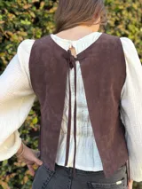 Chaleco de cuero marrón chocolate, sin mangas, con escote redondo y detalles de costuras decorativas en forma de espiga en el frente. Cuenta con cordones laterales para ajustar.