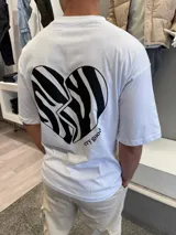 Remera blanca de corte oversize con estampa en la espalda de un corazón con diseño de rayas tipo cebra y la frase 'very good' en la parte inferior.