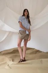 Camisa celeste a rayas verticales blancas, negras y grises, de corte recto y manga corta con dobladillo.