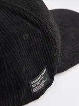 Gorra tipo baseball confeccionada en pana color azul marino, con parche rectangular lateral que incluye el logo de la marca Benson & Thomas.