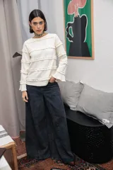 Blusa de color manteca con textura acanalada, cuello redondo y mangas largas con puños acampanados. El diseño presenta múltiples volados horizontales distribuidos a lo largo del cuerpo y las mangas.