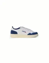 Championes Autry modelo Medalist Low, de estilo retro, confeccionados en cuero blanco con paneles de gamuza azul en la puntera y el talón. Presentan suela de goma color crema con efecto envejecido y el logo de la marca con la bandera estadounidense en el lateral.