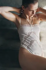 Body confeccionado en mezcla de seda con escote en pico y tiras ajustables al cuello con lazada. Presenta tirantes finos regulables y aplicaciones de encaje a tono en el frente y los bordes. Cuenta con cierre de ganchos en la espalda y botones a presión en el bajo.