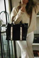Bolso tipo shopper color verde oliva, con doble correa de mano en cuero negro y detalles de cintas verticales con logo estampado. Cuenta con cierre superior, bolsillos laterales y un diseño espacioso ideal para uso diario.