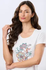 Remera blanca de manga corta con cuello redondo, confeccionada en algodón. Presenta una estampa frontal combinada con detalles bordados de flores en tonos verde, celeste y rosado.