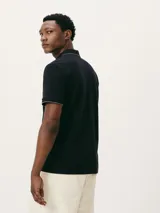 Chomba de manga corta color negro con cuello y tapeta interior en color gris claro. Presenta un pequeño bordado en el pecho y detalles de ribete en gris en el cuello y las mangas.