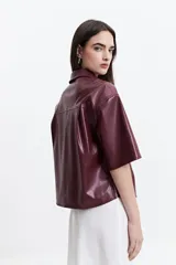 Camisa de manga corta confeccionada en cuero sintético color bordó, con cuello clásico, cierre frontal de botones metálicos y dos bolsillos frontales con solapa.