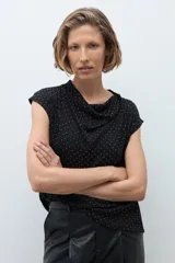 Blusa negra con pequeños puntos brillantes, cuello drapeado y mangas cortas.